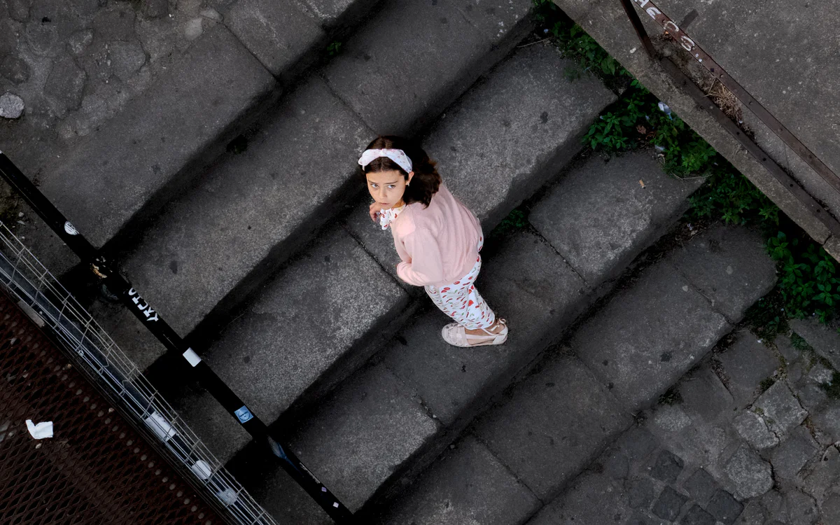 A child in a pink jumper looks up towards the camera from a stone step.