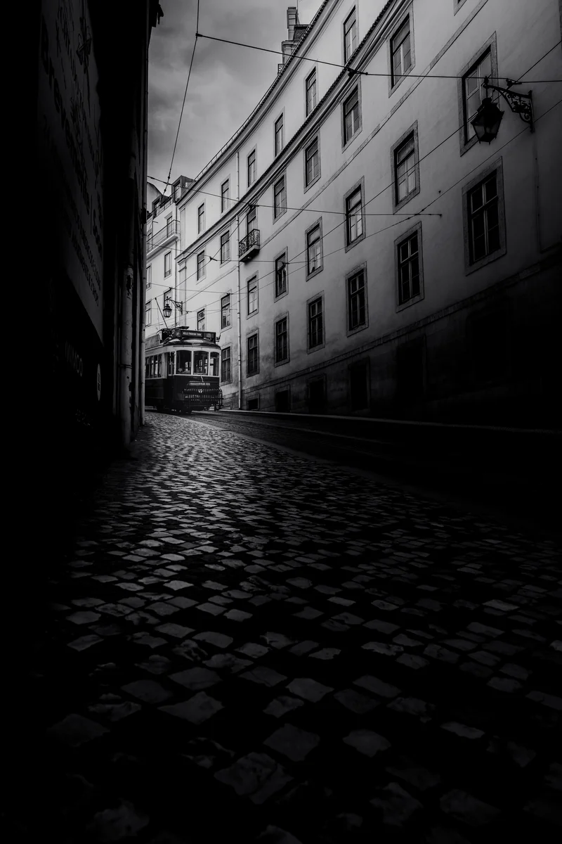 Black and white street scene with a tram emerging from shadow.