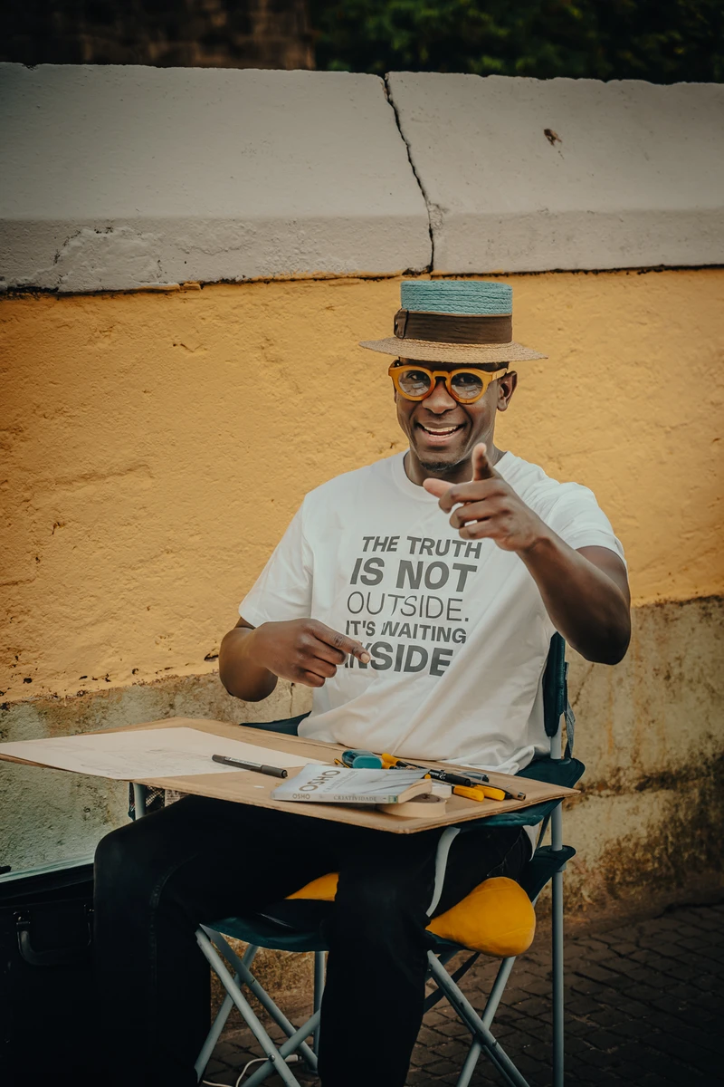 Smiling street artist Gaspar Silva with hat and “Truth is inside” shirt holding pen (Naeratav tänavakunstnik, pliiats käes, tõet-sõnum särgil)