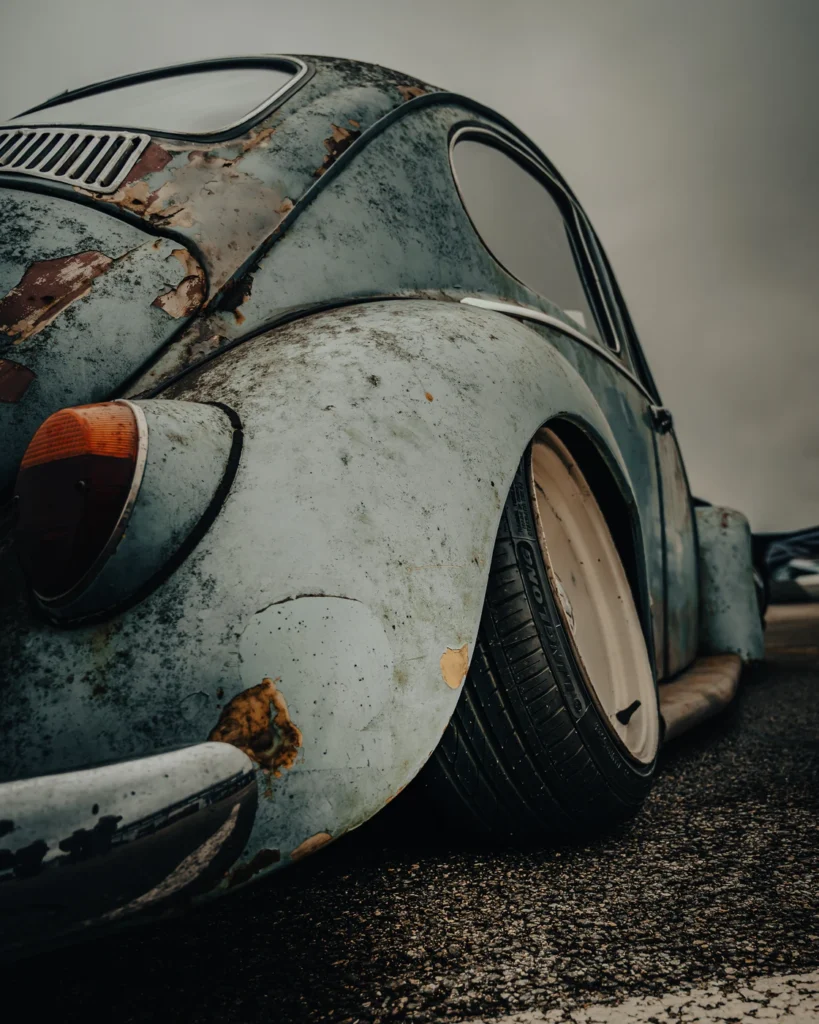 Rear wing of a Volkswagen Beetle with peeling paint and a wide pale wheel.