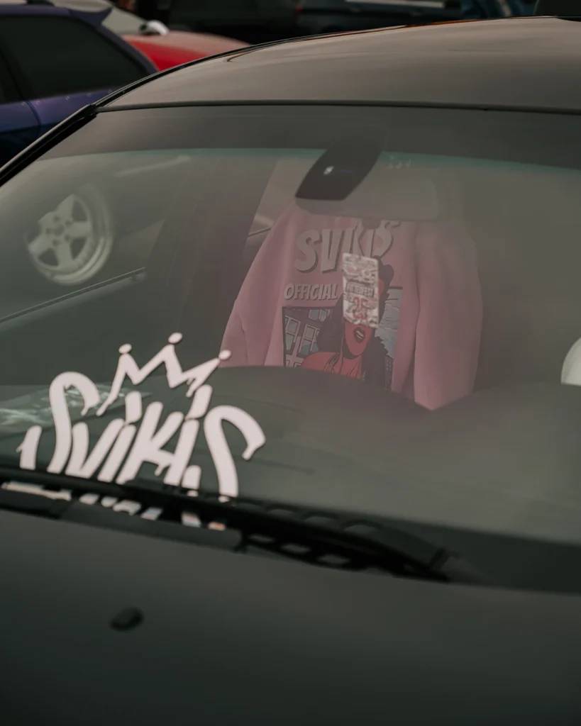 Car windscreen with Swik’s lettering and a pink shirt hanging inside.
