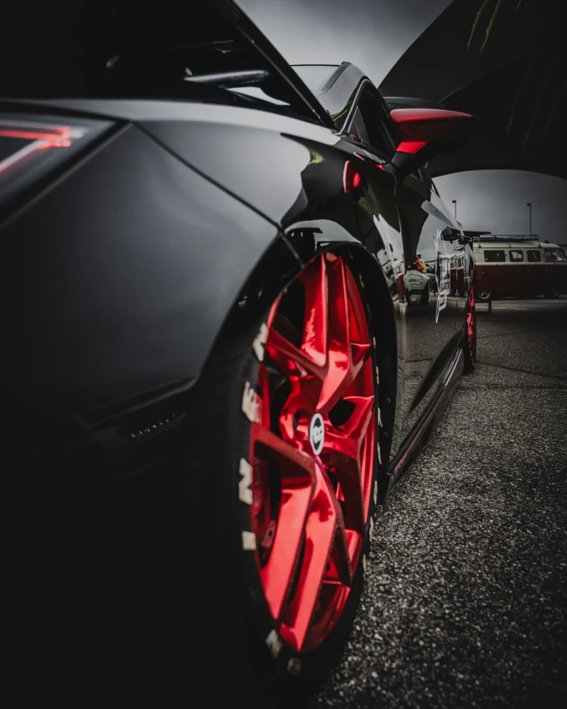 Glossy side of a black car and its red front wheel, with other festival cars behind it.