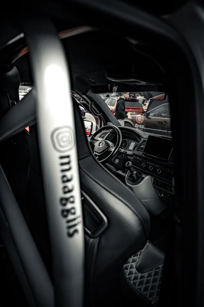 View over a black car seat towards the steering wheel, large screen and gear lever.