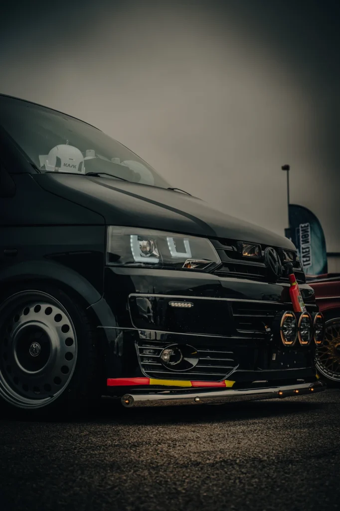 Front corner of a black Volkswagen van with a large wheel and colourful bumper trim.