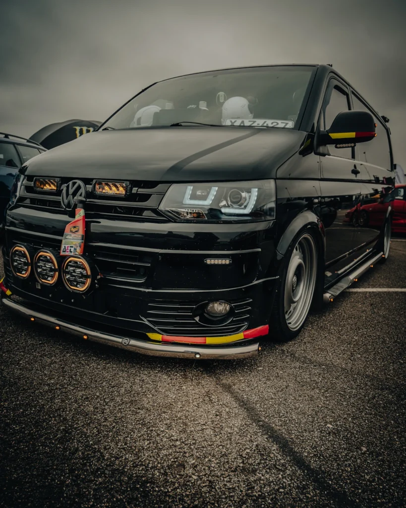 Front view of a black Volkswagen van with auxiliary lights and red and yellow bumper details.