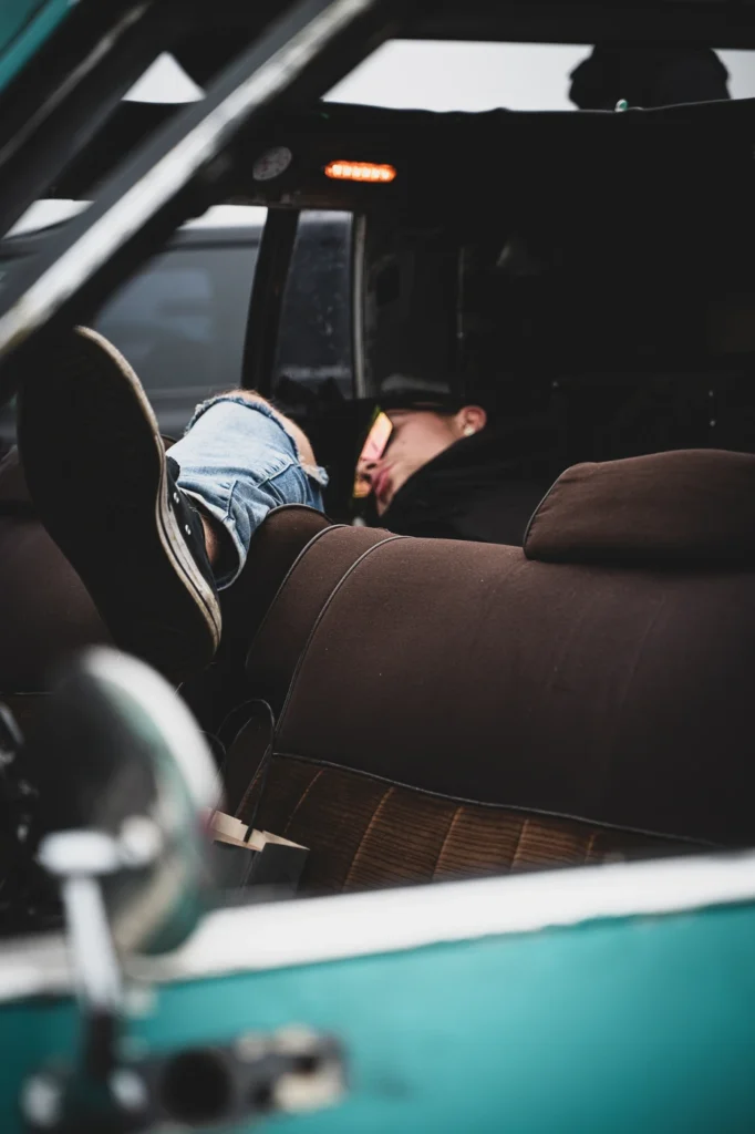 Brown seat and a resting visitor’s legs in jeans seen through an open car window.