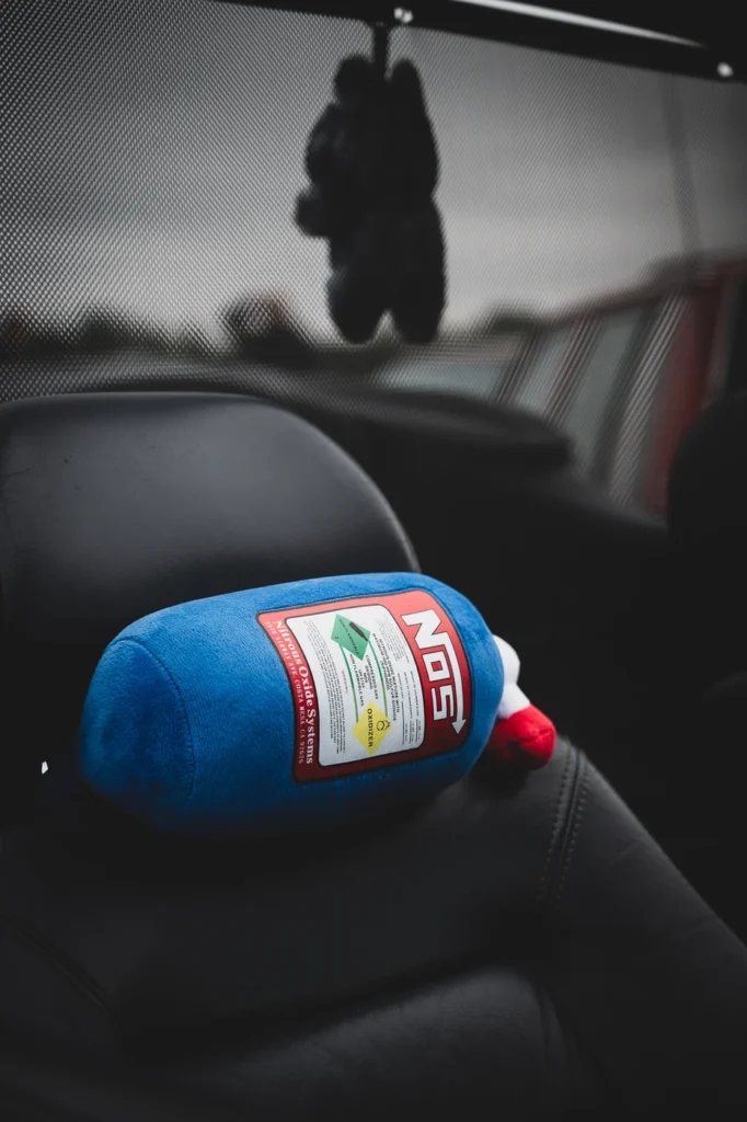 Blue soft toy shaped like a NOS bottle resting on a black car headrest.