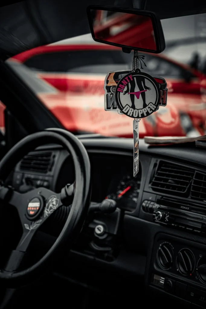 Air fresheners hanging from a rear-view mirror above a sports steering wheel and dashboard.