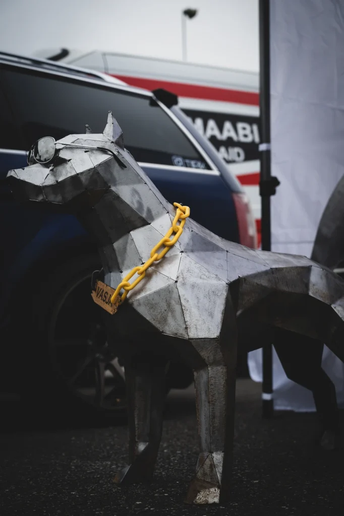 Faceted metal dog sculpture wearing a yellow chain and goggles on its head.