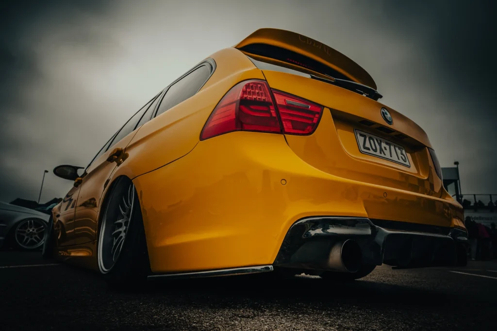 Rear view of a lowered yellow BMW with a large spoiler and wide exhaust pipe.