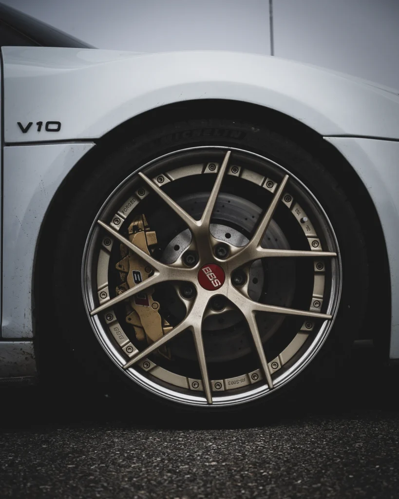 Front wheel of a white car with a bronze BBS rim, gold brake caliper and V10 badge.