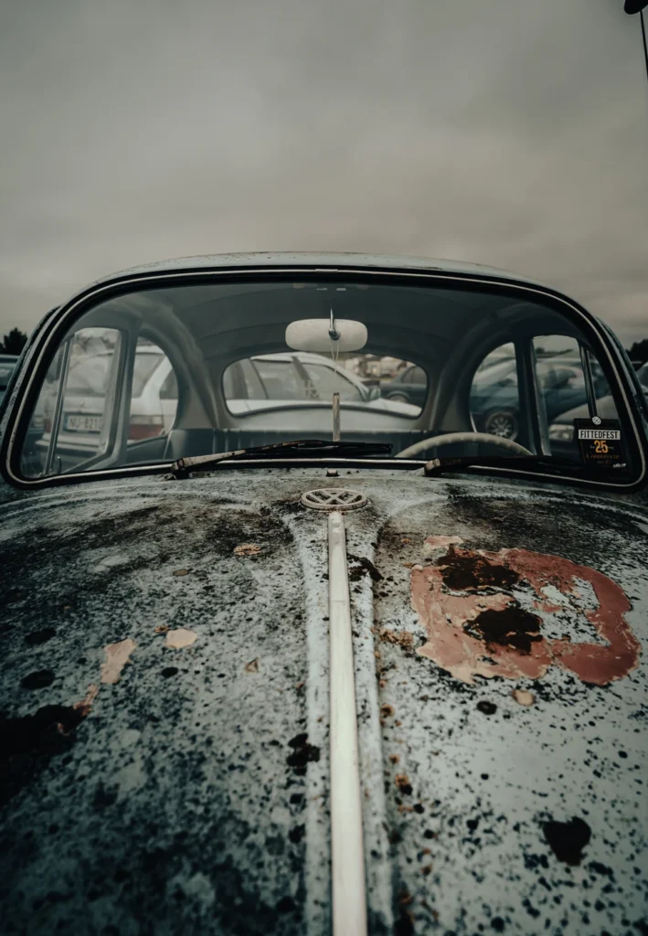 Weathered Volkswagen Beetle bonnet with a VW badge and chrome strip beneath the windscreen.