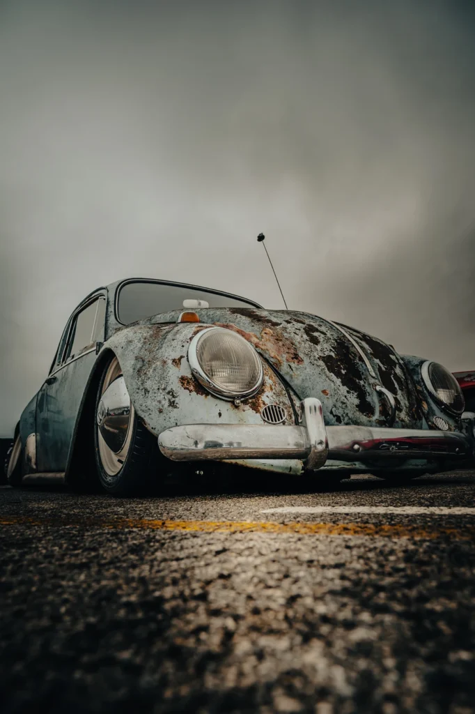 Lowered Volkswagen Beetle with a weathered finish, photographed from ground level under cloudy skies.