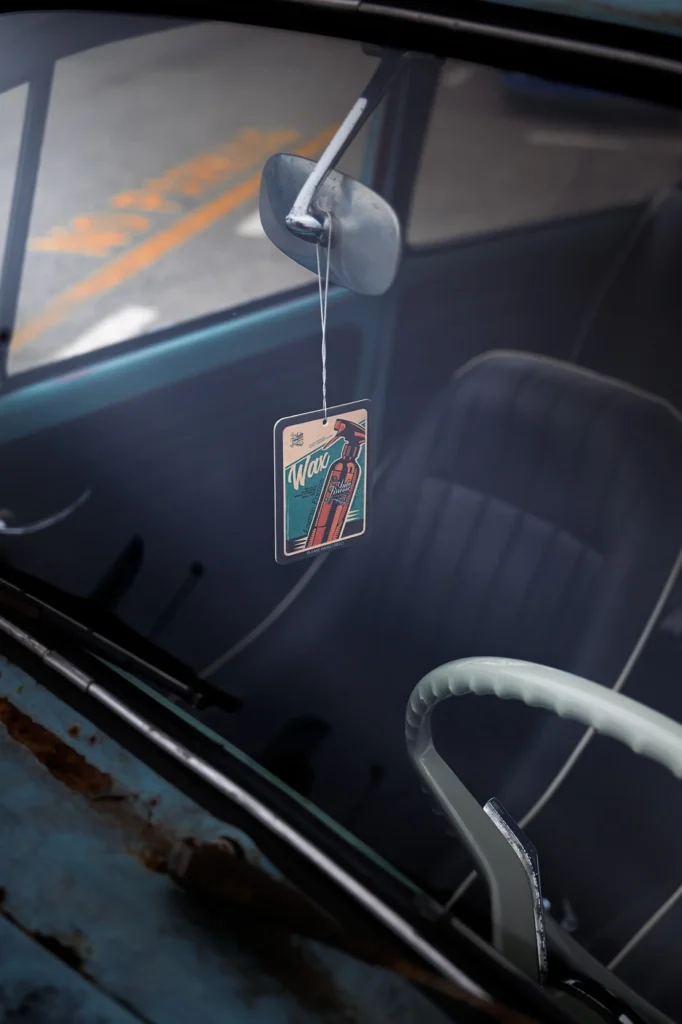 Vintage car interior seen through the windscreen, with an illustrated air freshener hanging from the mirror.