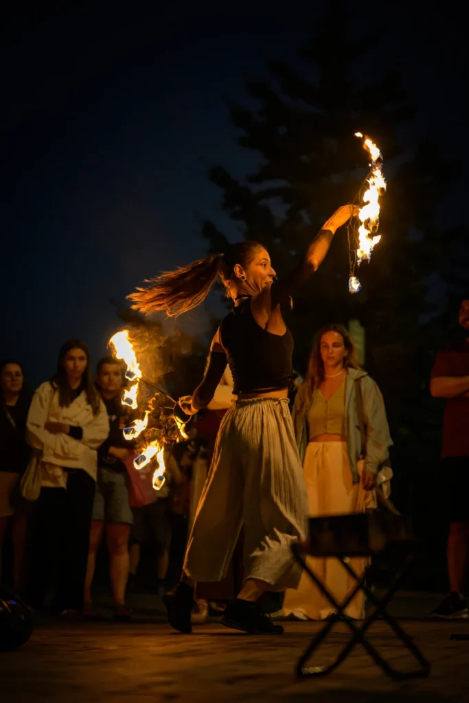 Natalia dances with two fire fans, one arm raised above her head and spectators behind her.