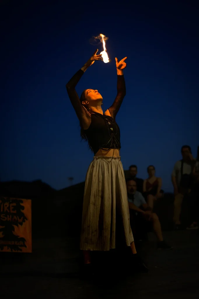 Natalia reaches both hands above her head and watches a flame against the blue evening sky.
