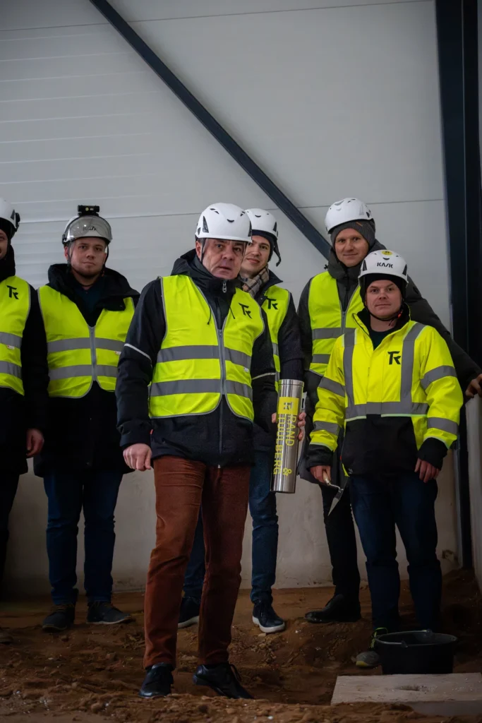 People in hard hats and safety vests pose with a cornerstone capsule and a trowel.