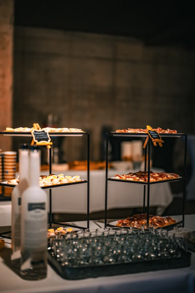Snacks on black serving stands and glasses on a tray on a white-clothed table.