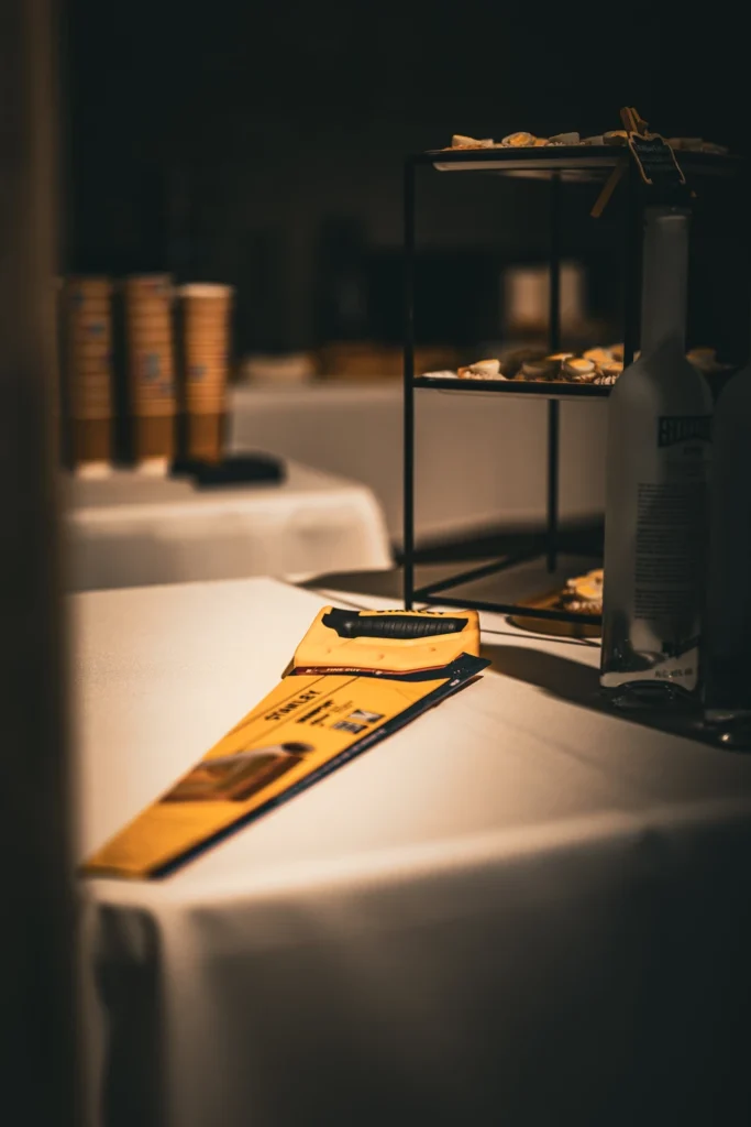 A yellow-handled hand saw on a white-clothed table beside snacks and a bottle.