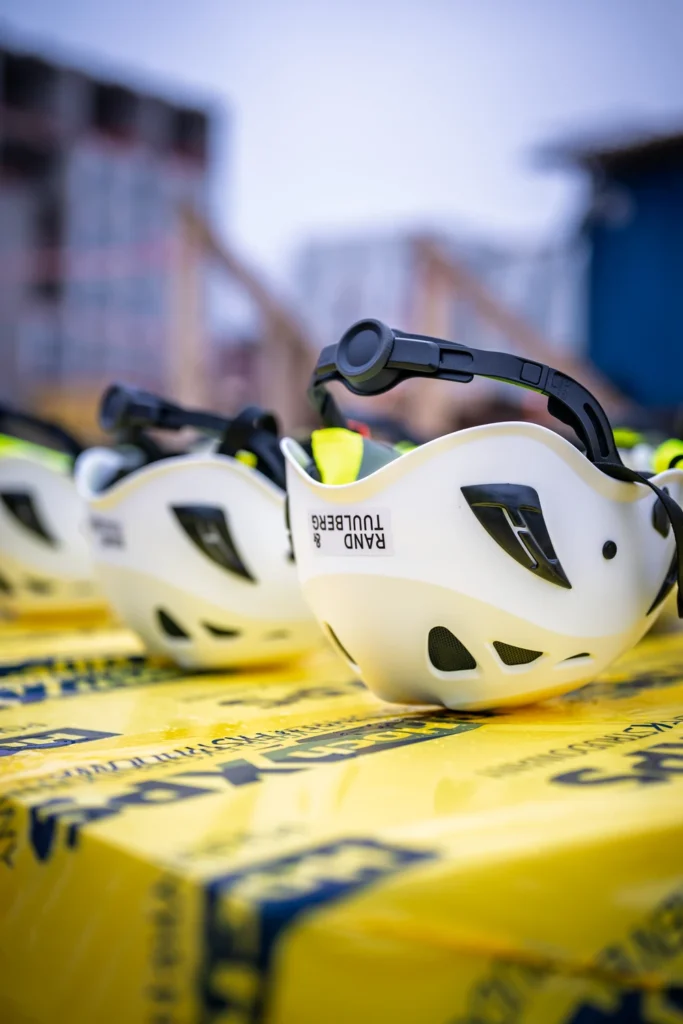 White hard hats on yellow-wrapped construction materials, with Rand & Tuulberg lettering on the nearest hat.