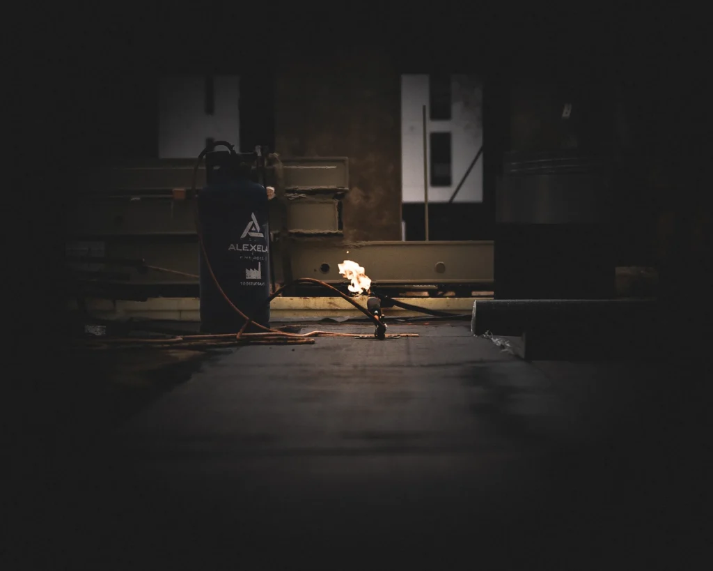 A gas cylinder and a lit gas torch on the floor of a dim room under construction.