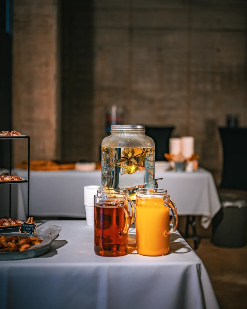 Two jugs of colourful drinks and a large dispenser with lemon slices on a refreshment table.