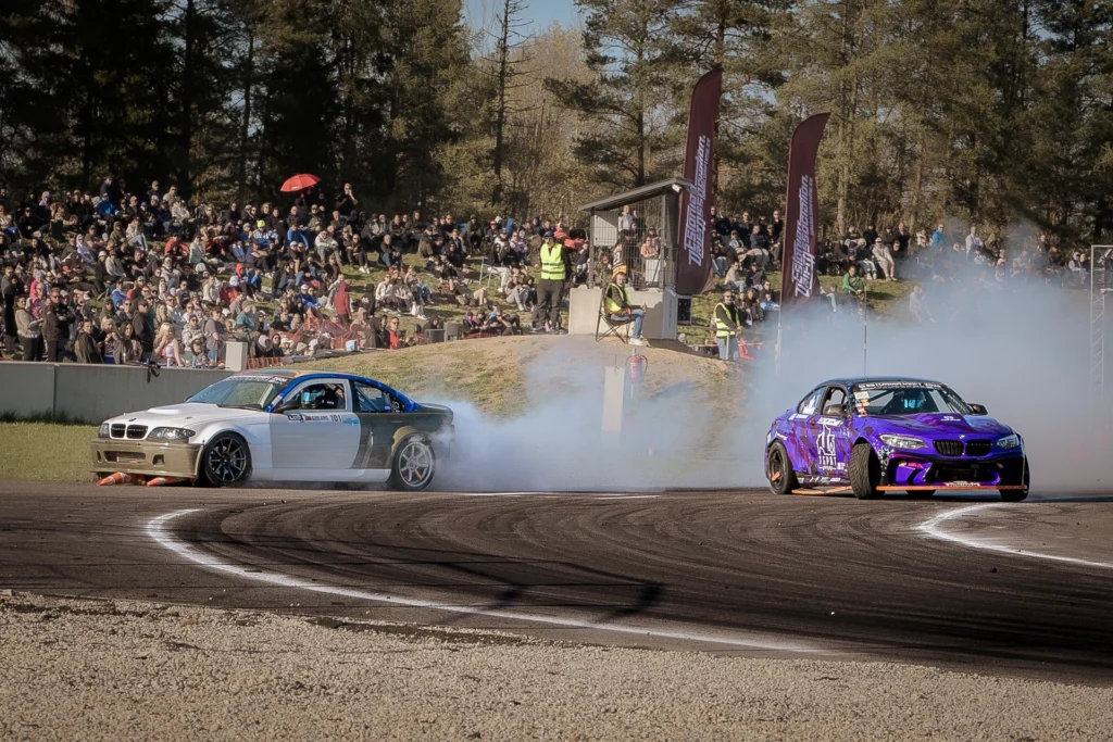 A silver car and a purple car drift at opposite ends of a bend marked with dark tyre tracks.