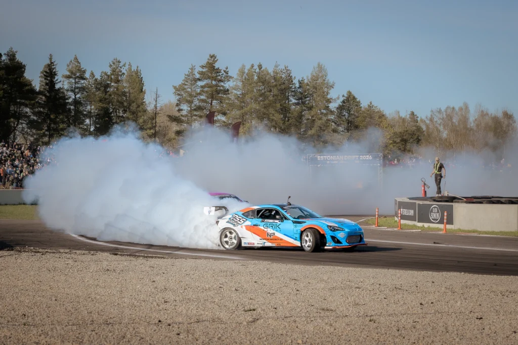 A blue-and-orange car with white wheels drifts in front of a thick smoke cloud.