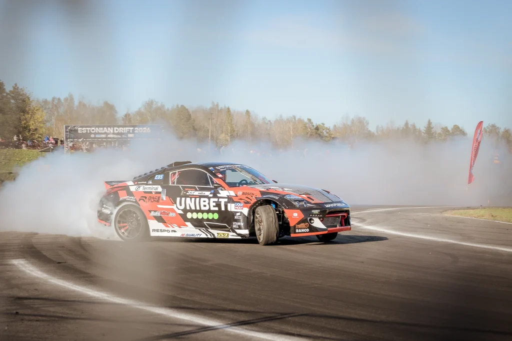 A car with red, black and grey racing graphics slides sideways across the tyre-marked track.