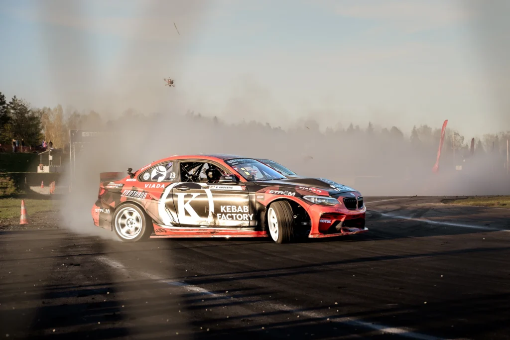 A red-and-black drift car with white wheels slides sideways through a corner.
