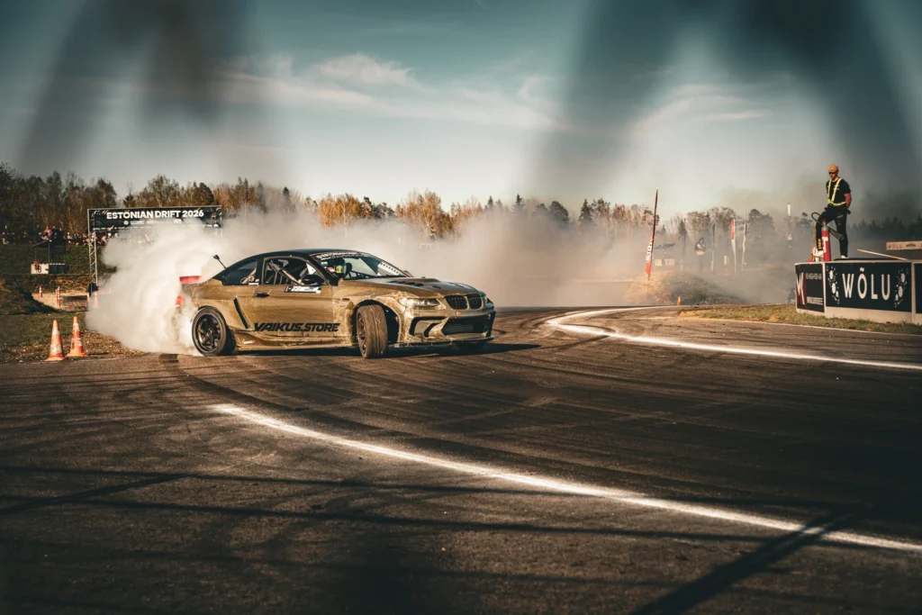 A gold drift car in a smoky corner, photographed through an out-of-focus fence.