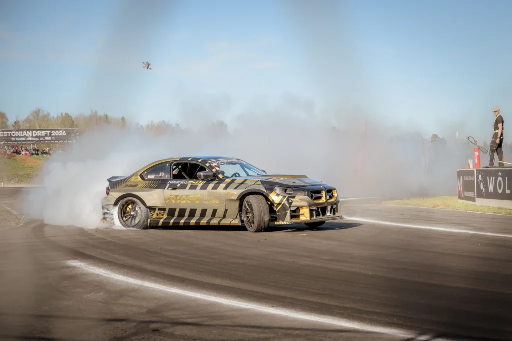 A black-and-gold drift car slides broadside through a corner, trailing smoke.