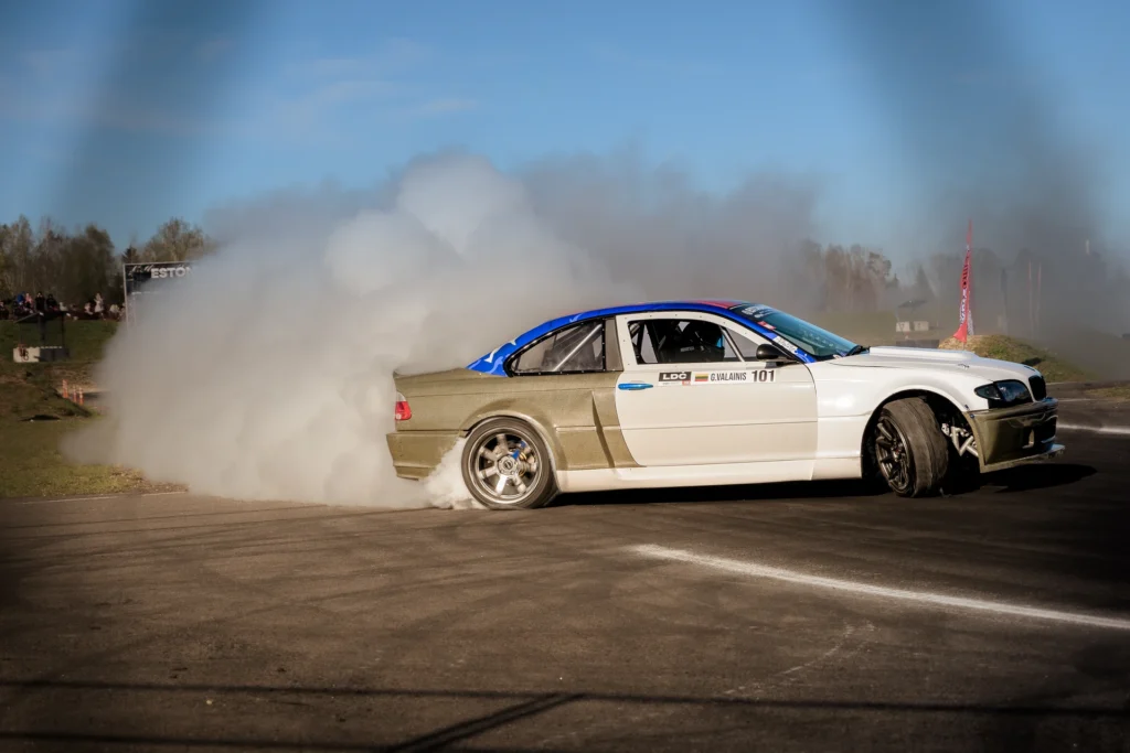 A drift car with a blue roof and white door slides sideways with white tyre smoke behind it.