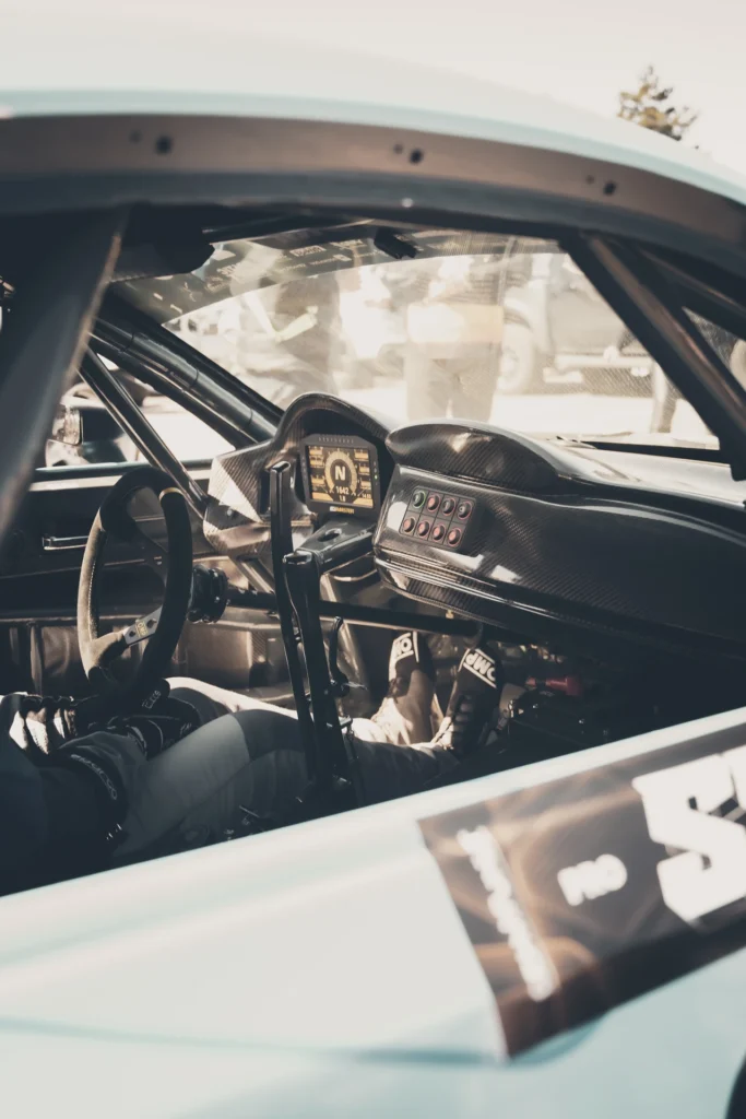 A drift car's cockpit through the side window, showing the steering wheel, roll cage and dashboard switches.