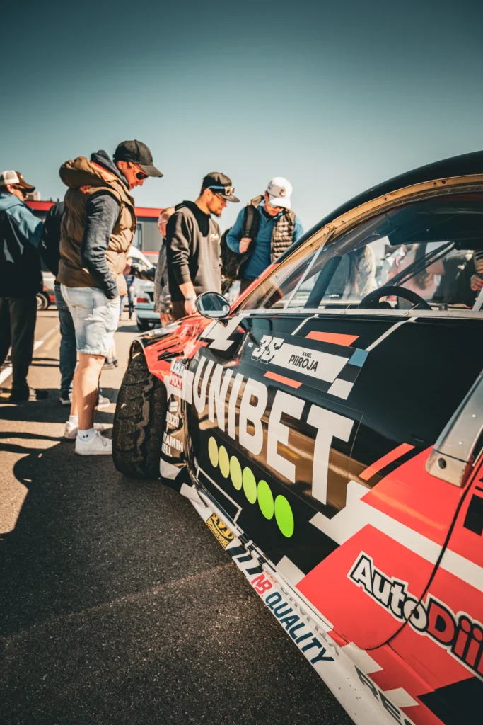Visitors look at a red-and-black racing car with its bonnet open.