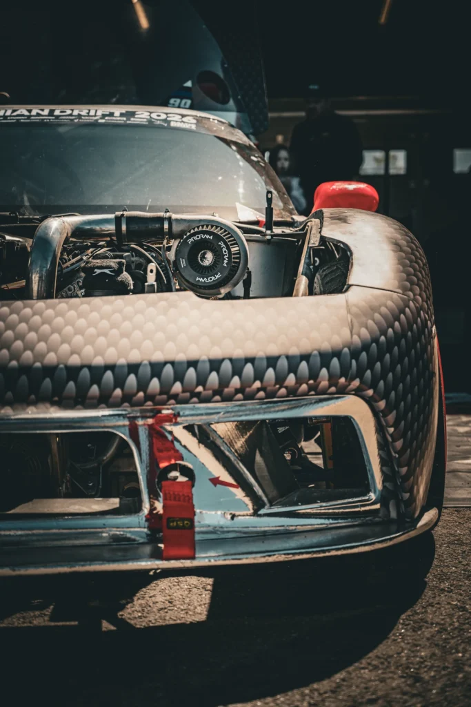 The front of a racing car with its bonnet removed and a red fire extinguisher standing in front.