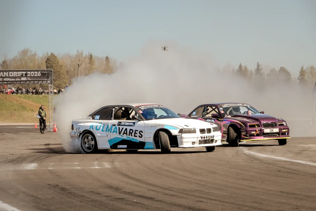 A white car and a purple car drift close together with their front wheels turned sideways.