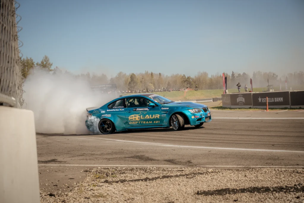 A turquoise drift car with black wheels slides sideways beside the track barrier.