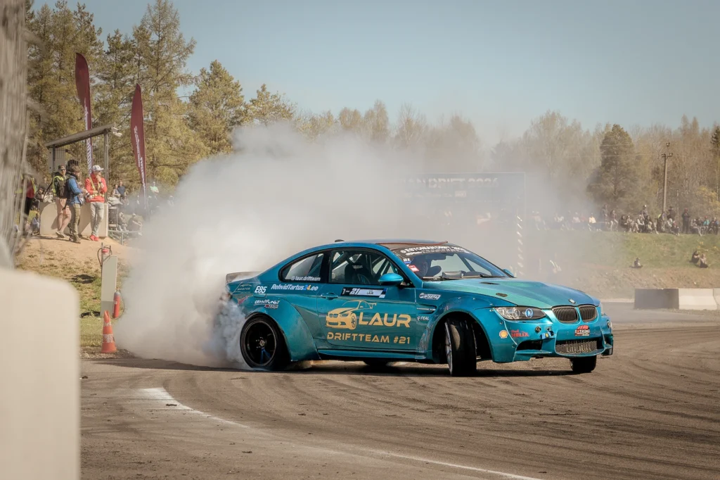 Front view of a turquoise drift car with countersteering front wheels and a smoky background.