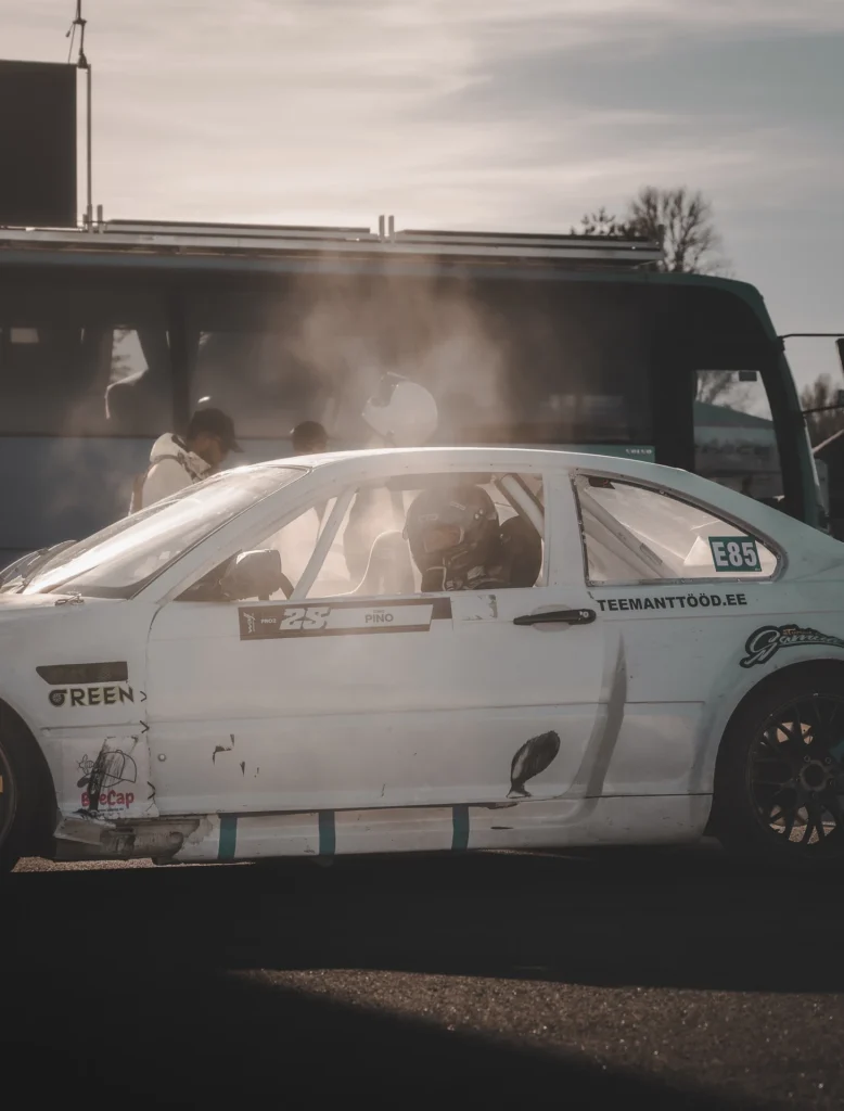 Side view of a white racing car in the paddock, with low sunlight shining through its roll cage.