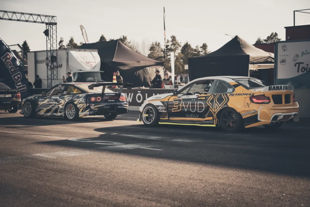 Rear view of two drift cars parked side by side in front of paddock tents.