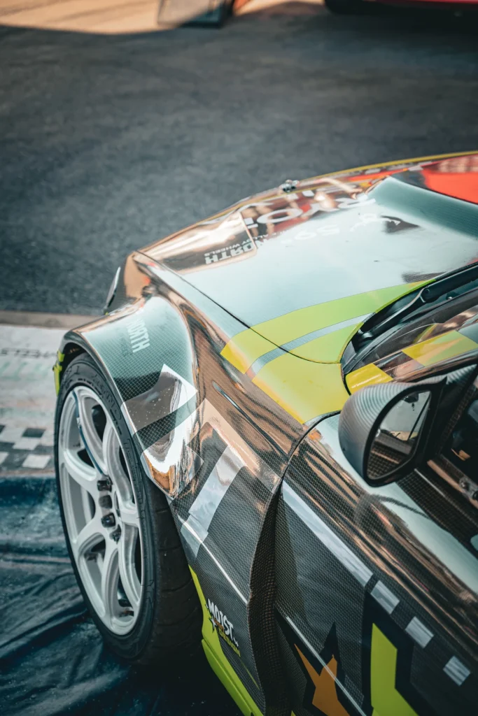 Close-up of a drift car's wide front wing, white wheel and bodywork with yellow accents.