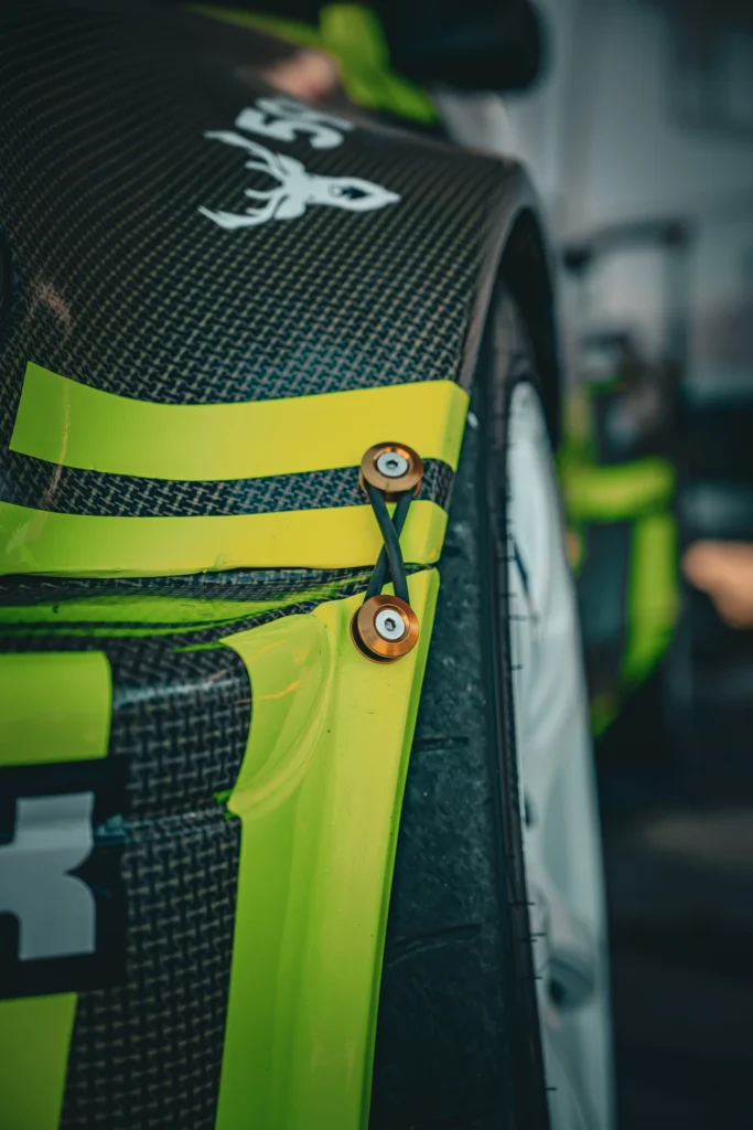Close-up of a fastener and wheel-arch edge on dark bodywork with a yellow stripe.
