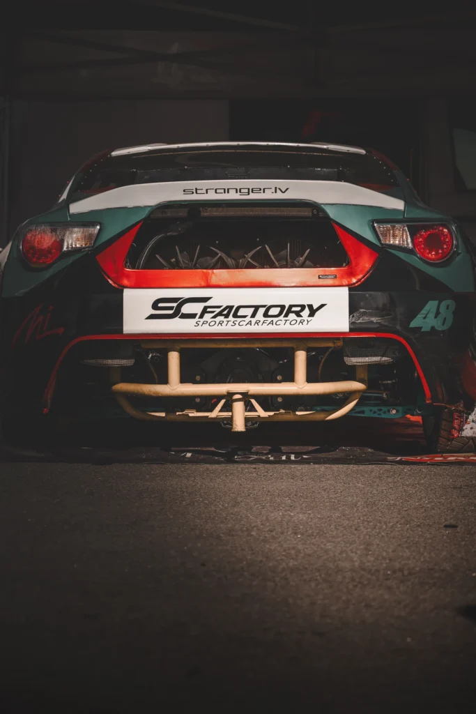 The open rear of a drift car with an exposed tubular frame in a dim pit bay.