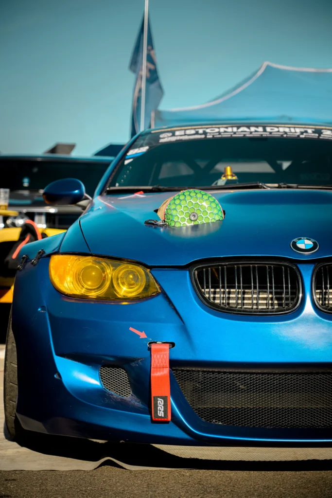 A blue drift car with yellow headlights, a green air filter protruding through the bonnet and a red tow strap.