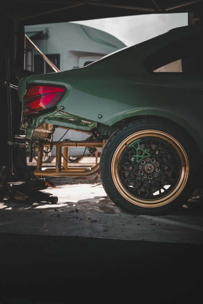 A green drift car's rear wheel and exposed tubing where the rear bumper has been removed in the pit bay.