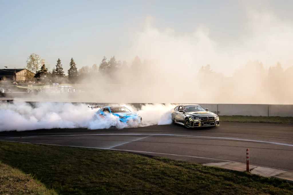 A blue drift car emerges from dense white smoke beside a black-and-gold car.