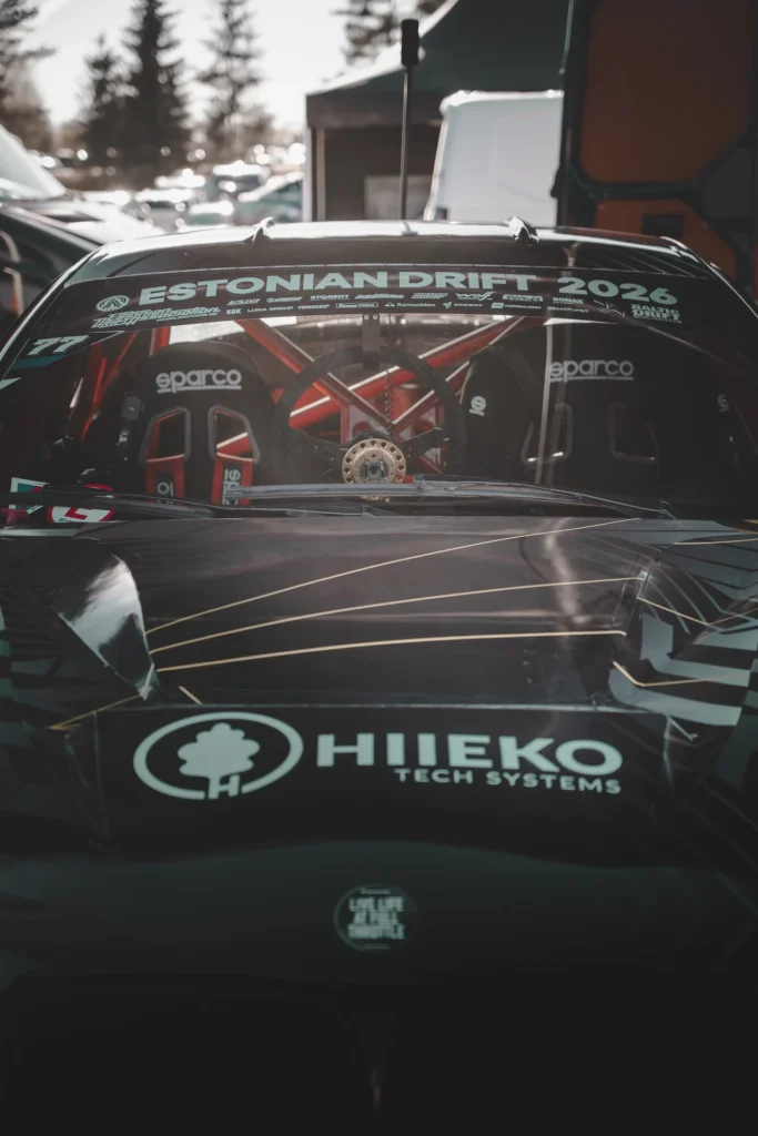 A dark drift car's bonnet and the red roll cage visible through its windscreen.
