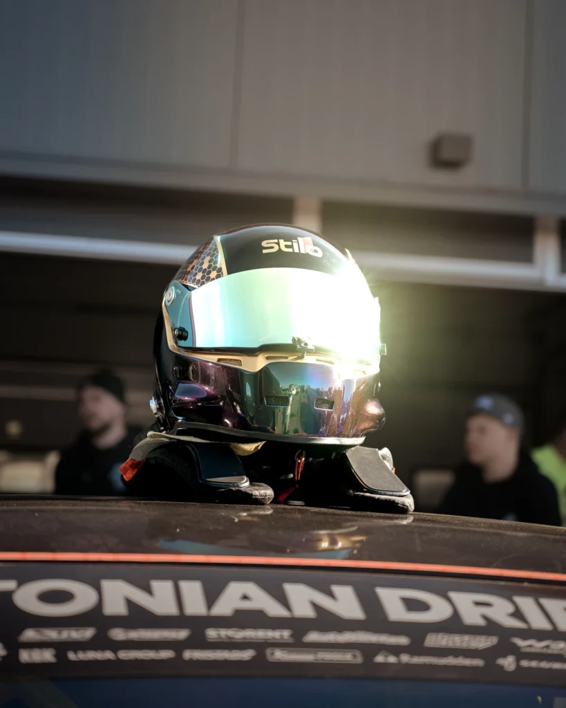 A racing helmet with a reflective green-tinted visor sits in a patch of sunlight on a car roof.