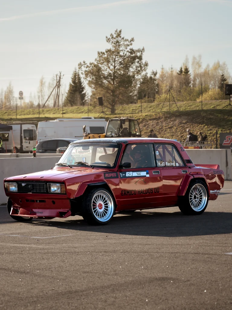 A red, boxy car with light-coloured wheels in the paddock.